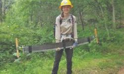 Crew member holds cross cut saw in front of forest